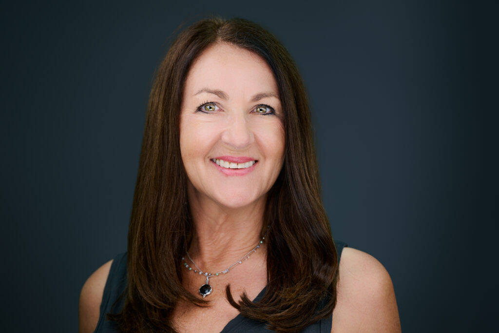 Professional headshot of a smiling businesswoman with long dark hair against a dark gray studio background in St. Louis, Missouri.