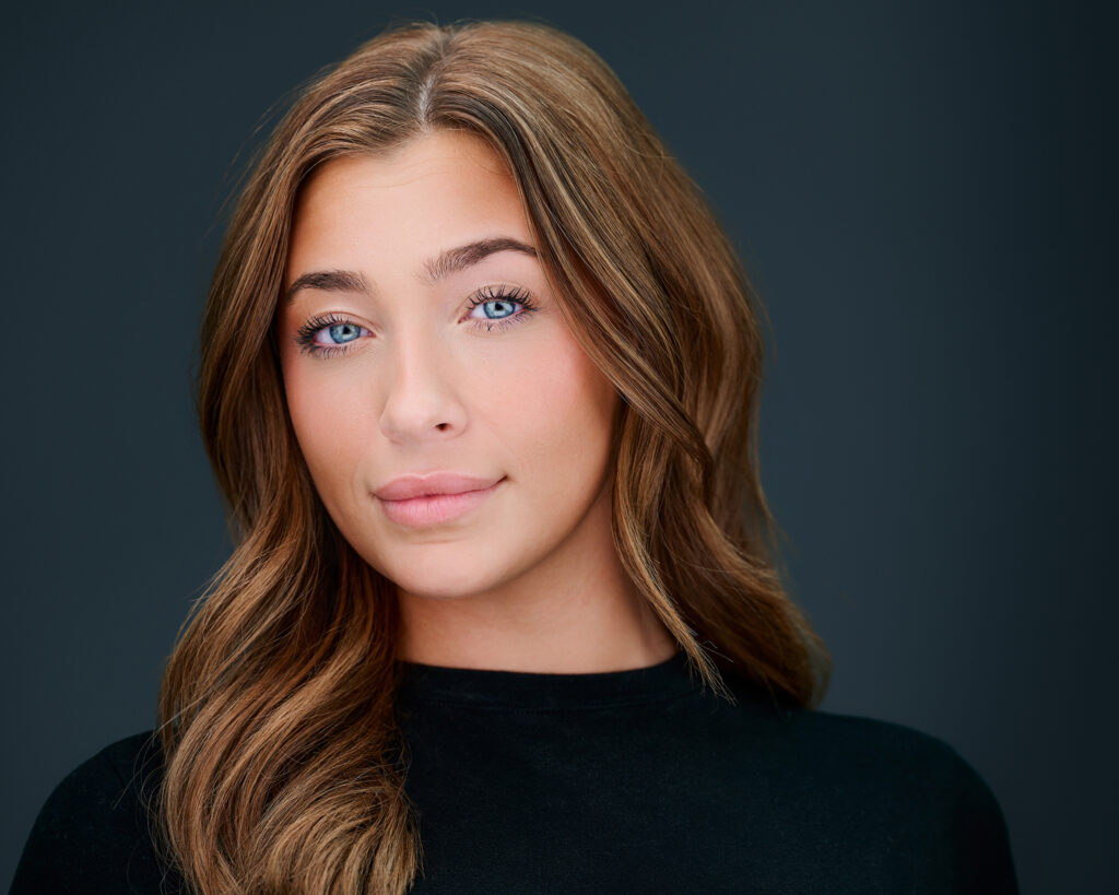 Professional headshot of a smiling hair and makeup artist against a dark gray studio background in St. Louis, Missouri.