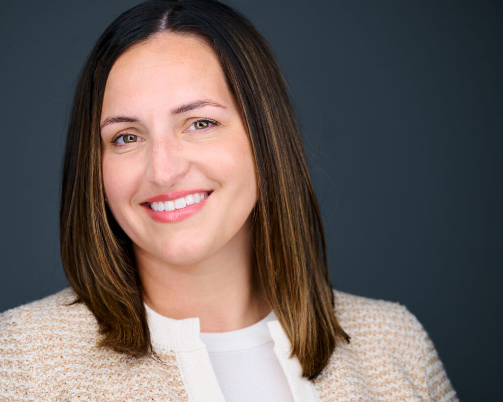 Professional headshot of a smiling human resources professional wearing a cream blazer against a dark gray studio background in St. Louis, Missouri.