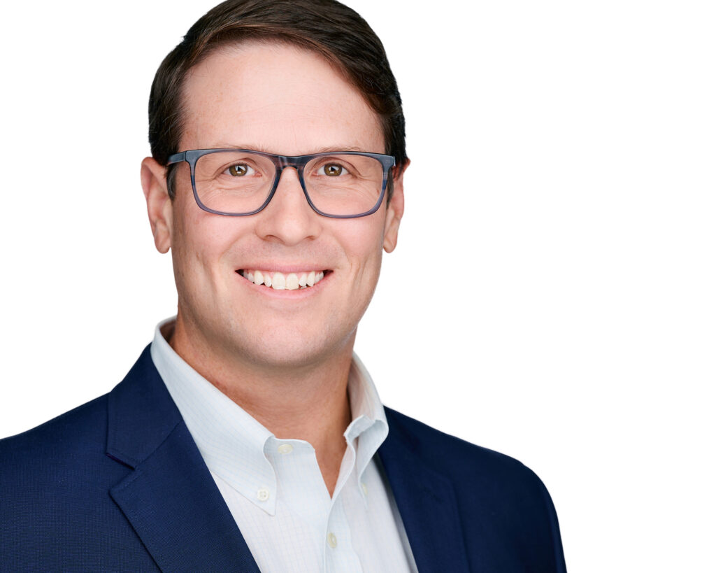Professional on-location executive headshot of a smiling businessman wearing glasses and a navy blazer against a bright office background in St. Louis, Missouri.