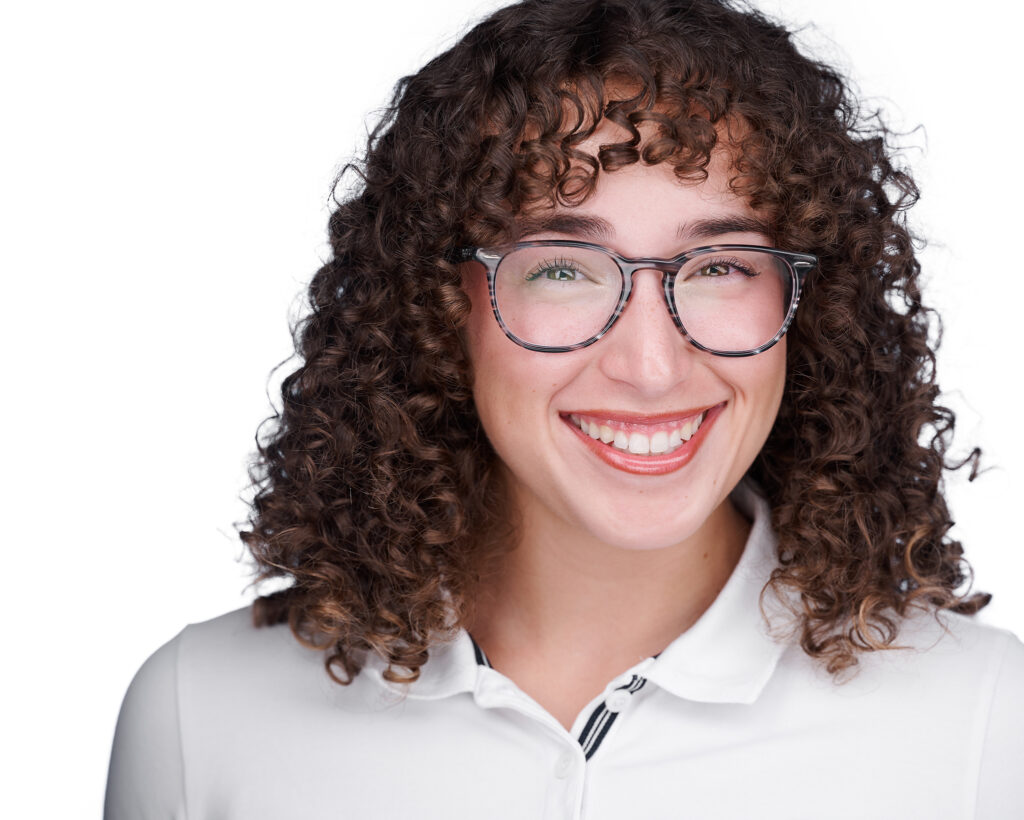 Professional headshot of a young man with very curly hair, large round glasses, and a bright smile wearing a white polo shirt, photographed with studio lighting in a St. Peters, Missouri studio serving the St. Louis area.