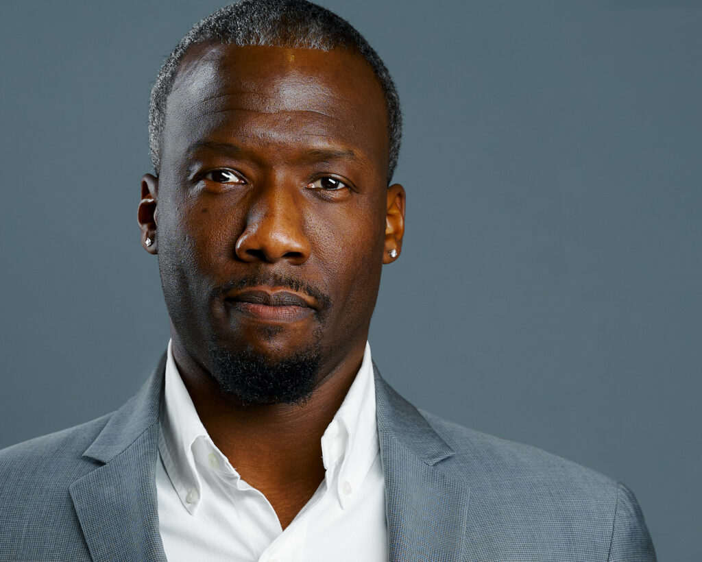 Executive headshot of a man in a gray blazer with a confident expression and blue-gray background